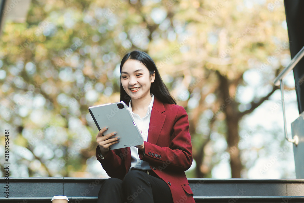 Fototapeta premium Focused woman in blazer types on laptop outdoors. Urban professional works remotely on stairs. She uses modern tech for business and connection.