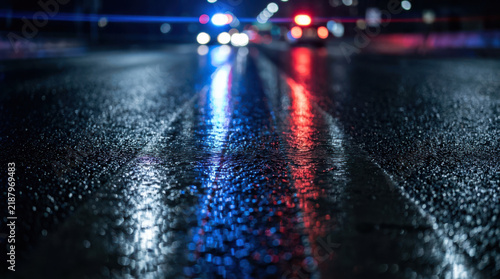 Police cruiser reflection asphalt street night light blur wet scene captured under emergency vehicle glare, highlight rain soaked roadway texture