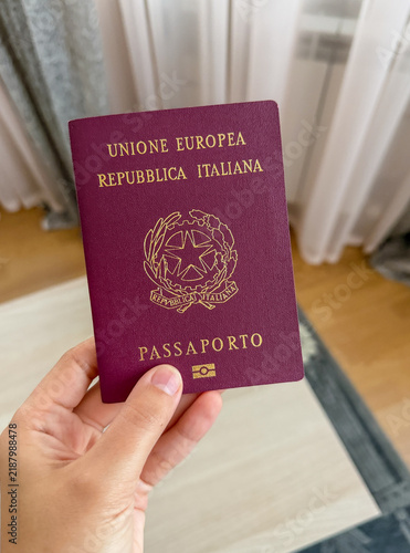 Fotografie Close-up of a person holding an Italian passport near a window, representing Ita