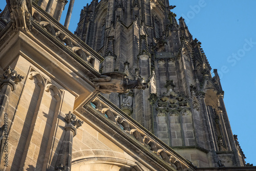 Low-angle close-up of stone gargoyles and intricate Gothic pinnacles on St. Vitus Cathedral in Prague Castle, Czech Republic.