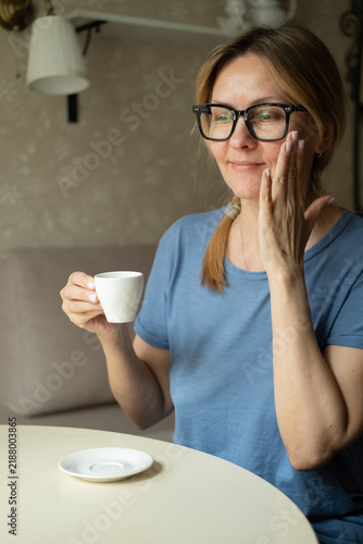 Foto Happy dreamy middle aged woman is staying in living room with cup of black tea or coffee, looking away, Peaceful mature lady enjoying no stress calm positive pastime alone at home