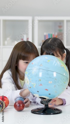 Two Young Schoolgirls in Lab Coats Studying a World Globe
