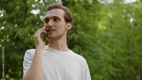 Cheerful young adult making a phone call outdoors on a nice summer day.