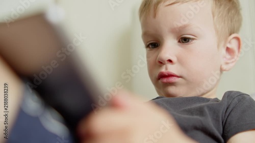 Close-up of a small boy focused on a digital tablet screen at home. Little child watching a cartoon on an iPad.