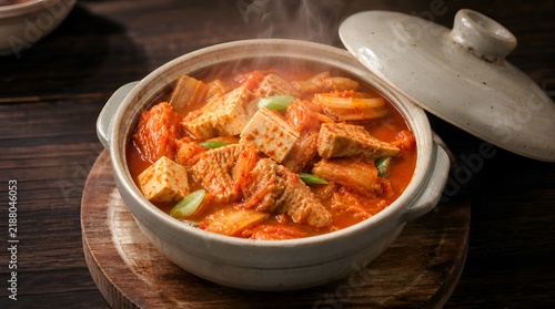 Hot steaming Kimchi-jjigae stew with tofu in traditional clay pot. Authentic spicy Korean soup on rustic wooden background.