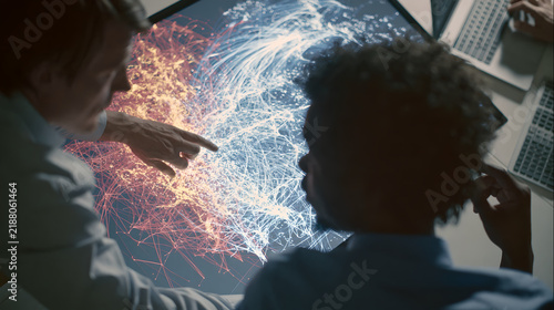 Two professionals analyzing complex data network visualization on digital screen while working together in modern office