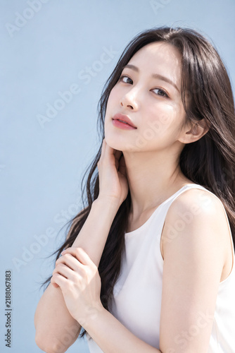 Naklejka 淡いブルー背景で首元に手を添えるロングヘアの日本人女性の上品な美容ポートレート