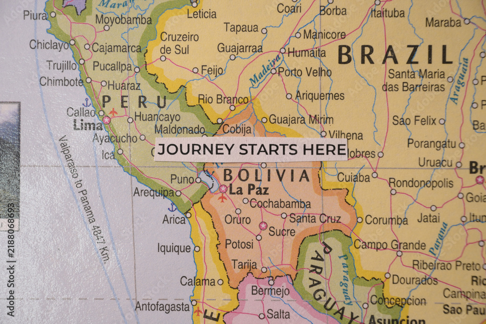Obraz premium Overhead shot of a handwritten paper tag reading journey starts here resting on a physical map of Bolivia