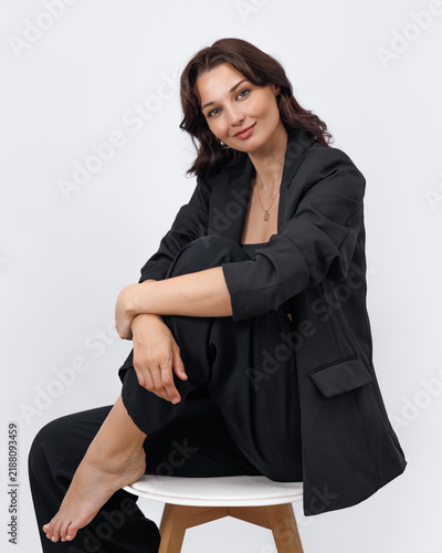 Confident Young Woman in Black Business Suit Sitting on White Stool