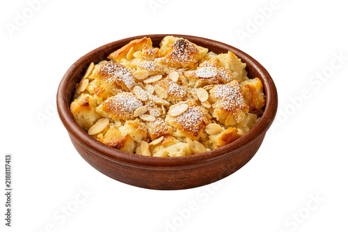 Traditional Egyptian dessert Umm Ali served in a brown ceramic bowl, topped with golden baked pastry pieces, sliced almonds and powdered sugar, isolated on transparent background.