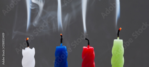 Fotografie Extinguished four candles in white, blue, red and green with smoke rising from burnt wicks