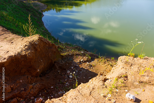Obraz na plátně Steep clay bank of an abandoned quarry overlooking a serene pond with mirror-lik