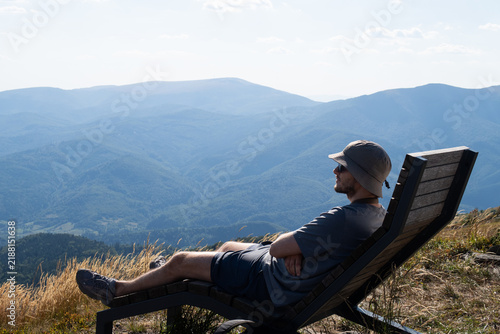 A man lies on a mountain ridge on a wooden deckchair