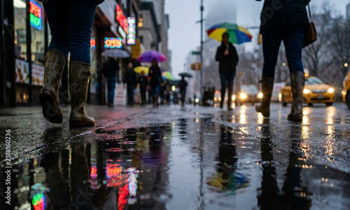 A rainy city street scene featuring pedestrians with umbrellas and reflections on the wet pavement, capturing the atmosphere of urban life in inclement weather.