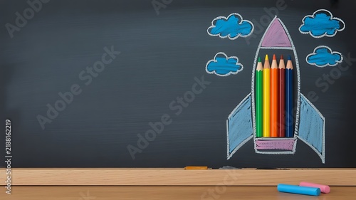 Colorful pencils arranged inside a rocket shape drawn with chalk on a dark blackboard with clouds and wooden frame for creative education concept