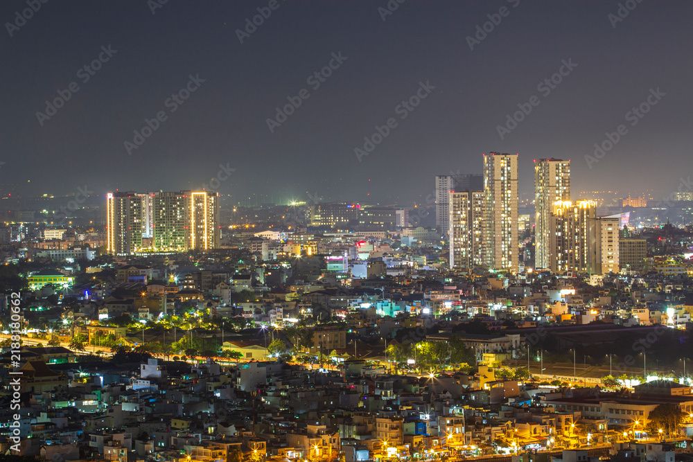 Fototapeta premium A panoramic view of a densely built urban skyline illuminated by streetlights and building windows beneath a dark night sky.