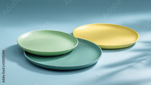 Three colorful ceramic plates in pastel green dark turquoise and soft yellow resting on a light blue surface