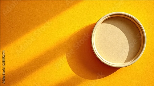 Round paper cup lid on a bright vibrant yellow textured background with strong shadows