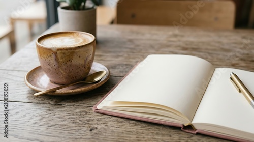 Hot cappuccino with latte art and open notebook on a rustic wooden table