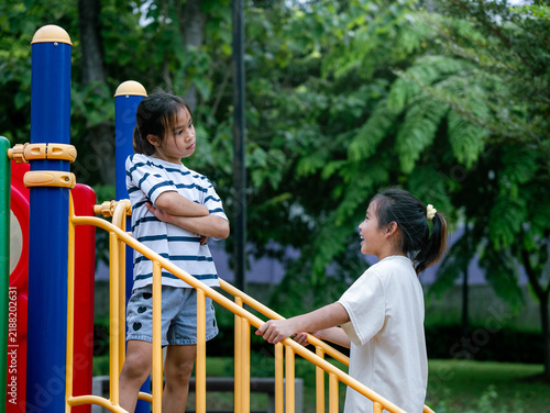 Foto Stubborn Asian girl with crossed arms sulking on playground stairs while sister