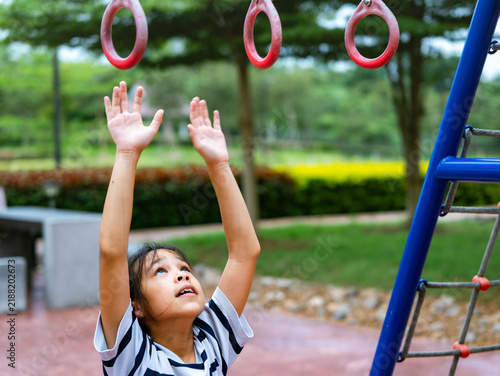 Foto Asian little girl reaching up hands trying to grab gymnastics hanging rings at o