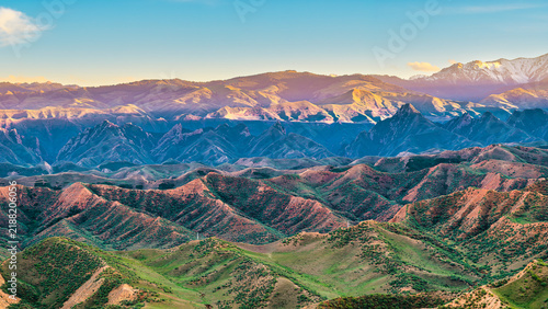 Fotografía An aerial view of layered mountain ranges in Xinjiang under soft sunlight, displaying green vegetation, steep ridges, and distant peaks