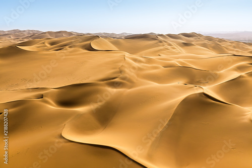 Foto Vast golden sand dunes stretching across the desert landscape under bright sunlight and a clear blue sky in Xinjiang, China