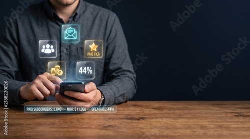 Smartphone with glowing subscriber analytics and paid membership metrics displayed as futuristic glass panels in dark business setting with warm wooden desk and clean copy space