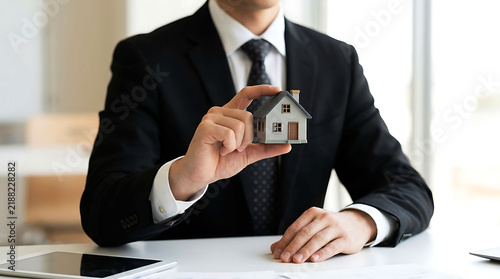 Real estate agent holding a model house in office showing property investment