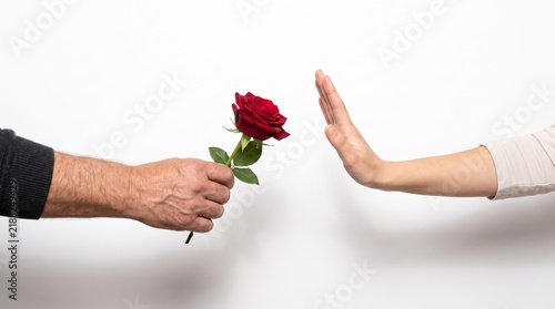 Close up of a man hand offering a red rose while a woman hand makes a stop gesture to reject the romantic gift, concept of unrequited love and relationship conflict isolated on a white background
