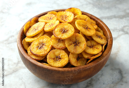Crispy fried plantain chips served in a wooden bowl on a marble surface for a healthy snack option