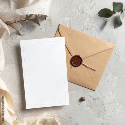 Blank white stationery card with craft envelope and wax seal, textured stone background, wedding invitation mockup