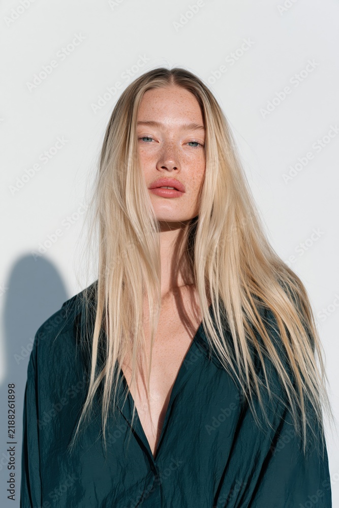 Fototapeta premium Natural light portrait of a freckled blonde woman with long hair wearing a deep green blouse for beauty portrait background and fashion banner