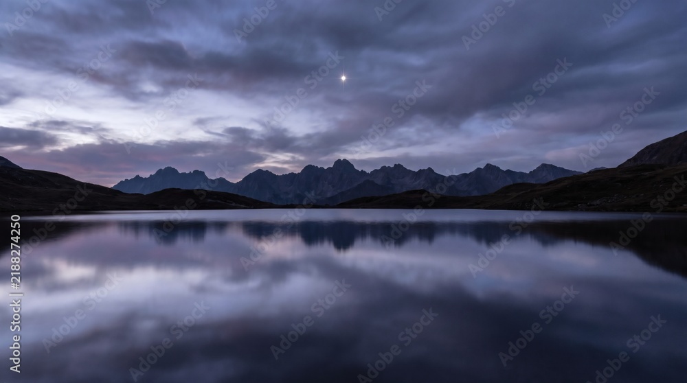 Fototapeta premium Bright Star Reflecting in Calm Alpine Lake under Twilight Cloudy Sky