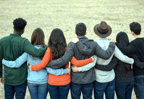 Group of diverse friends standing together with arms around each other showing unity and friendship outdoors