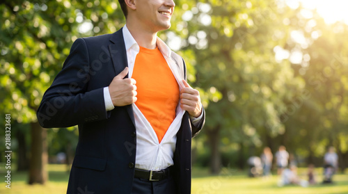 Smiling Man in Suit Reveals Vibrant Orange Superhero Shirt in Sunny Park