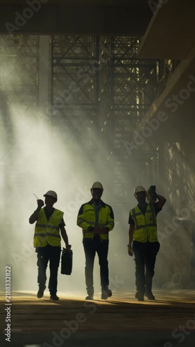 Vertical Screen. Building Construction Site with Workers. Three Construction Workers Walking Toward Camera Inside a Large Commercial Real Estate Building Site, Carrying Tools and Equipment 
