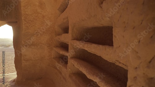 Interior view of an ancient Nabataean rock-cut burial chamber with wall niches and sunlight entering through the entrance in Hegra, AlUla