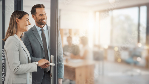 Business partners unlocking door to new office with blurred corporate space background banner.