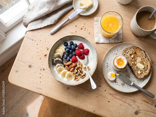 A delicious and healthy breakfast spread featuring yogurt, fresh fruits, nuts, and toast with a soft-boiled egg