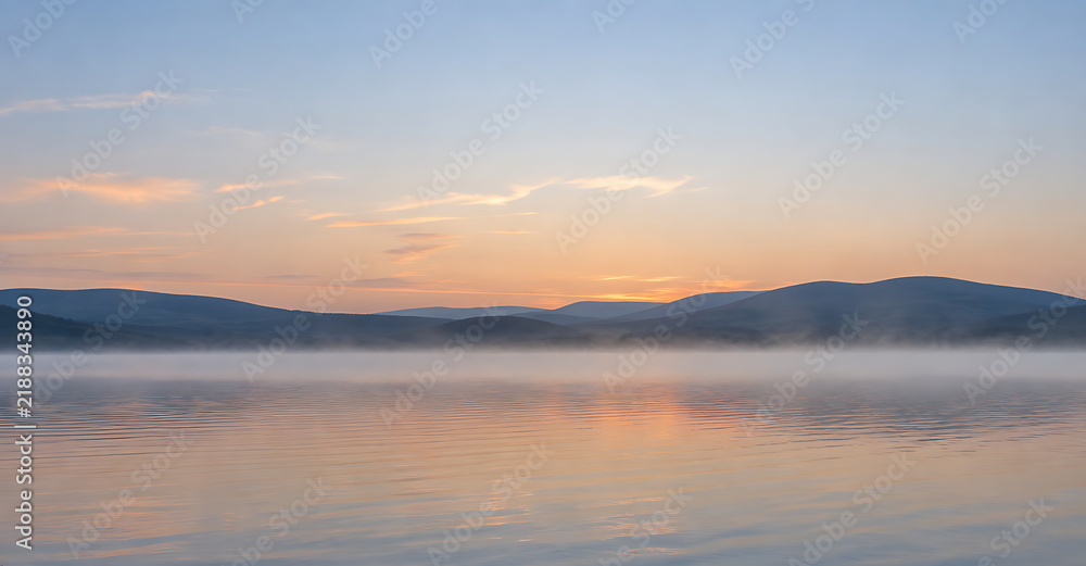 Fototapeta premium Morning mist drifting over a calm lake at pastel dawn
