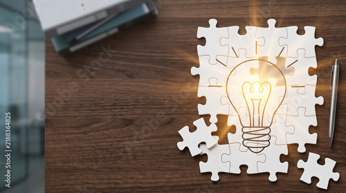 Glowing light bulb drawn on white puzzle pieces on wooden office desk for business idea concept