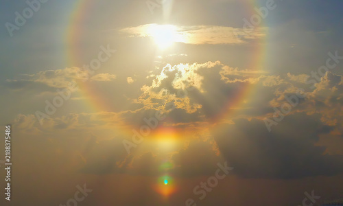 Bright sunlight shines above layered clouds in a golden sky, with a large colorful lens flare and glowing cloud edges creating a warm atmospheric scene. Background with copy space