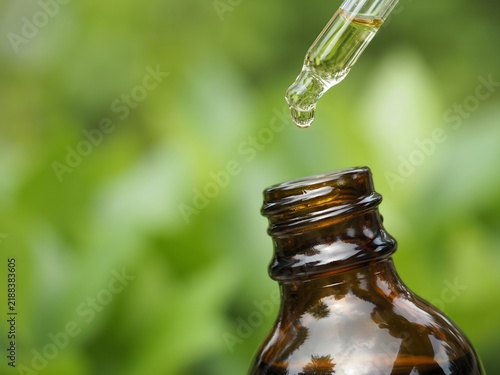 Close-up of a dropper releasing liquid into a small glass bottle in natural outdoor setting
