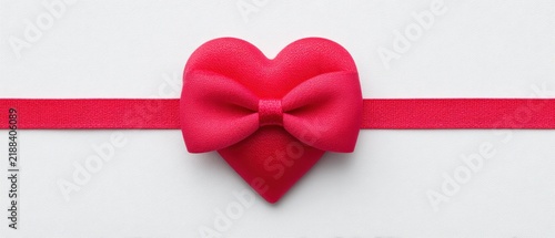 A detailed view of a vibrant red heart adorned with a delicate bow set against a pristine white backdrop representing love and affection perfect for celebrations such as weddings or valentine's day