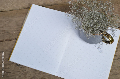 Open dotted notebook with delicate baby's breath flowers in a golden rimmed cup