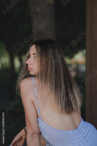 Quadro su tela Sensual young woman in an open-back light blue dress turning her head to look over her shoulder in a dark park setting
