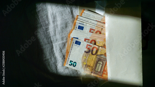 Konstfotografi Stack of 50 euro banknotes partially hidden in envelope under dramatic shadow, suggesting cash payment, hidden money, shadow economy, tax evasion, corruption, bribery and illegal financial activity