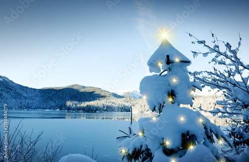 Christmas tree with lights and mountain reflection in the lake.