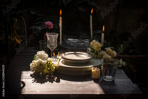Spooky Halloween candlelight dinner table setting with burning candles, empty plate, crystal glass, and dark vintage atmosphere for a creepy gothic party or haunted mansion concept. 